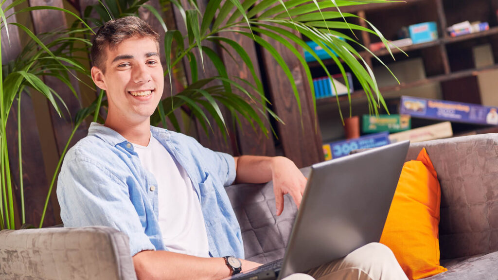 Junger Mann sitzt auf einer Couch mit einem Laptop auf dem Schoß